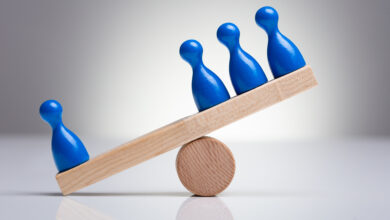 Blue Pawns Figures Balancing On Wooden Seesaw Over The Desk