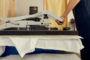 Cropped shot of male worker using heat press transfer machine for printing t-shirt. Printing on clothing and textiles concept. Horizontal shot. Side view