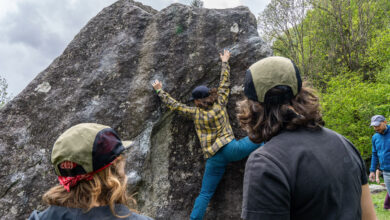group of people watch as person boudlers on rock face - atlantis